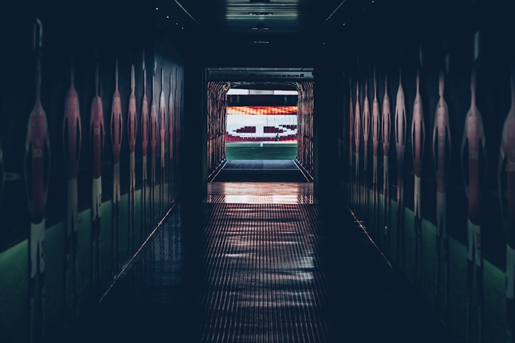 现代化大型足球体育场内景，绿色草坪与红蓝彩色座椅交相辉映，顶棚结构宏伟